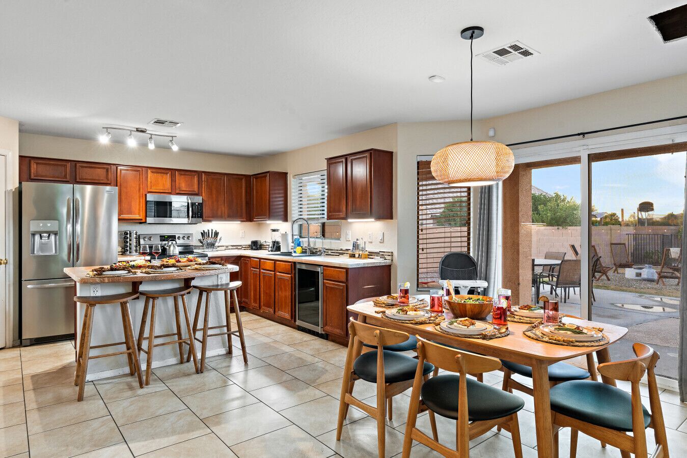 A modern kitchen with a dining area, stainless steel appliances, and a large window overlooking a backyard.