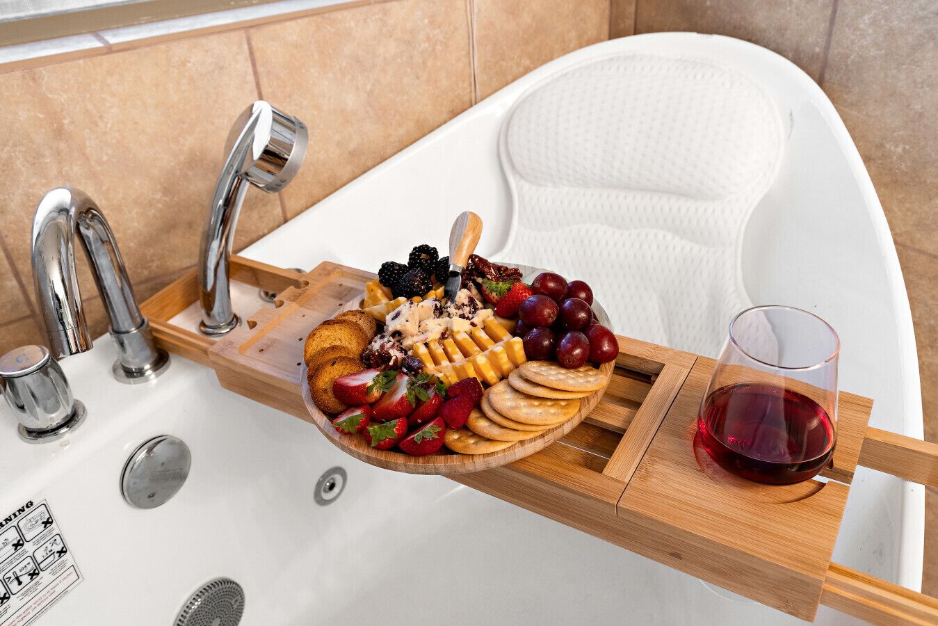 Une salle de bain avec une baignoire blanche, un plateau en bois contenant des collations et un verre de vin rouge, ainsi qu’un robinet.