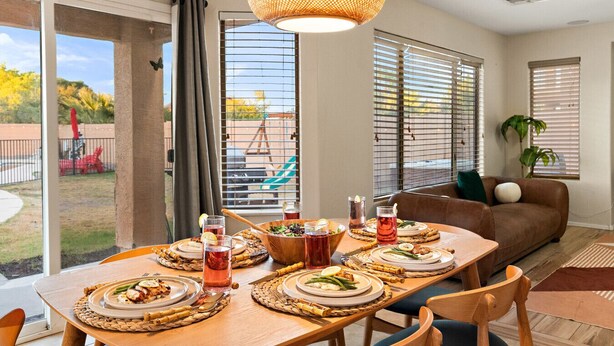 A dining area with a table set for four, a brown sofa, and a large window with blinds.
