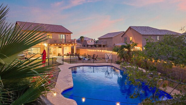 A swimming pool surrounded by houses with a patio area and string lights. - Pause & Play | Pool, Spa, Gaming, Firepit & More (Casa Grande)