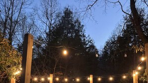 A fire pit surrounded by wooden chairs, string lights, and a stone border. - Creekside Dome with Firepit (Carroll County)
