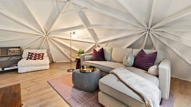A modern living room with a geometric ceiling design, a sofa, ottoman, and a coffee table. - Creekside Dome with Firepit (Carroll County)