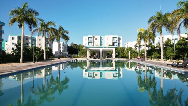 A swimming pool with clear water reflecting the surrounding buildings and palm trees. - Luxurious Punta Cana Apartment Comfort, Convenience, and Caribbean Charm (Punta Cana)