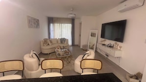 A living room with a sofa, chairs, a coffee table, a TV, and a mirror. - Luxurious Punta Cana Apartment Comfort, Convenience, and Caribbean Charm (Punta Cana)