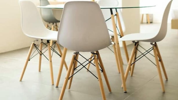 Een moderne eetruimte met een glazen tafel, witte stoelen met houten poten en een lichtgekleurde vloer.