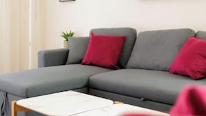 Een moderne woonkamer met een grijze modulaire bank, een klein houten tafeltje en een schilderij van een zonsondergang.