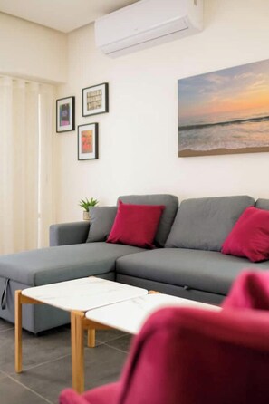A modern living room with a grey sectional sofa, a small wooden table, and a painting of a sunset. - PINO · Loft in ground floor - 1 block to El Llano Park (Oaxaca de Juárez)