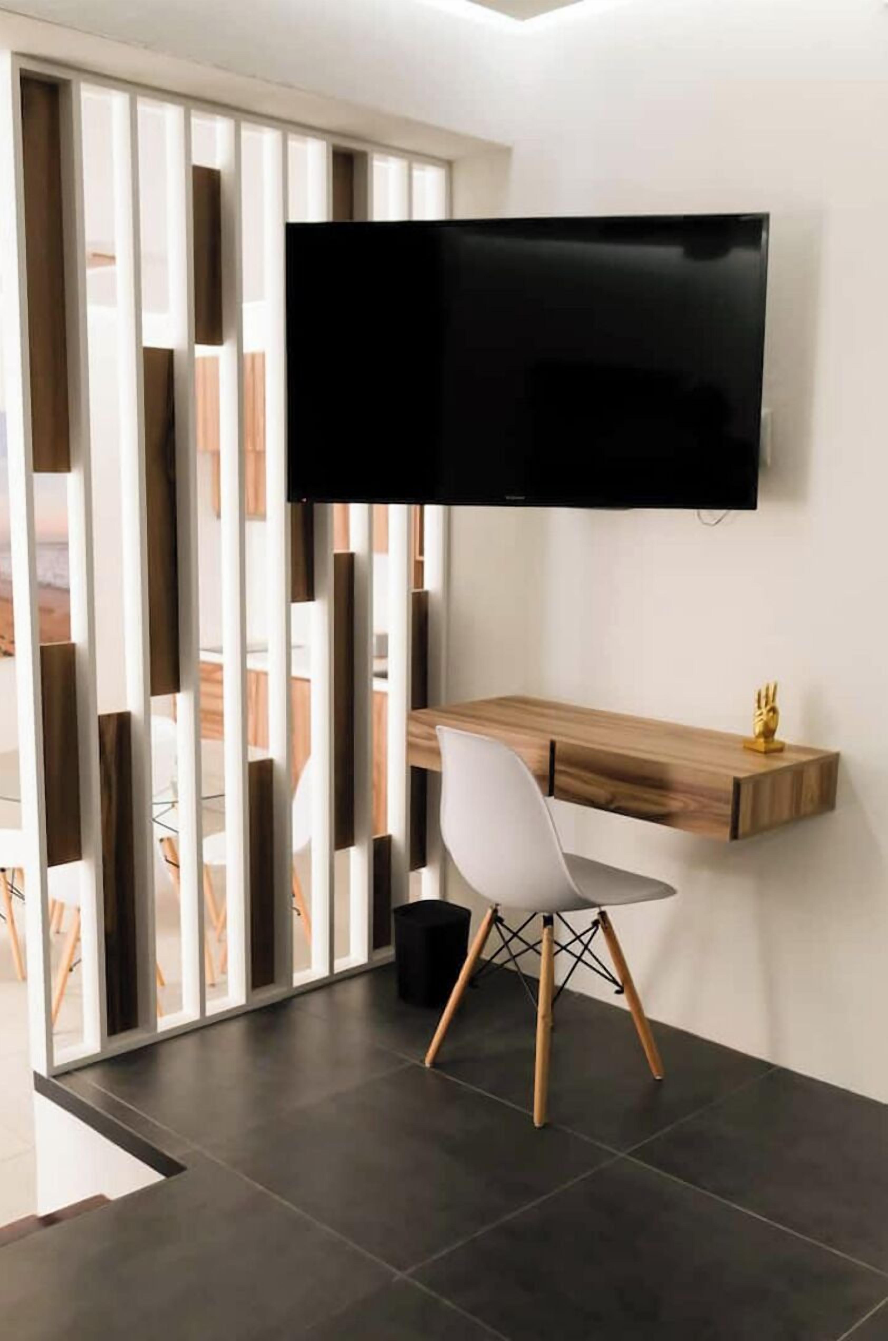 Een moderne kamer met een bureau, stoel en een wandgemonteerde televisie.