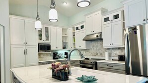 Uma cozinha moderna com armários brancos, geladeira de aço inoxidável, bancada de mármore e iluminação pendente.