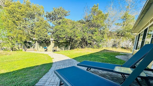 Um pátio com duas cadeiras de descanso, um caminho pavimentado e uma área gramada com árvores.