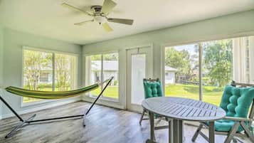 A room with a hammock, a round table, teal chairs, and large windows.
