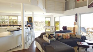 Ein modernes Interieur mit Küche, Essbereich und Wohnbereich, gekennzeichnet durch eine hohe Decke und große Fenster.