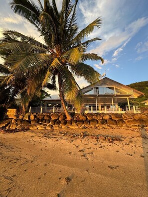 A beachfront property with a stone wall, palm trees, and a building with a sloped roof.
