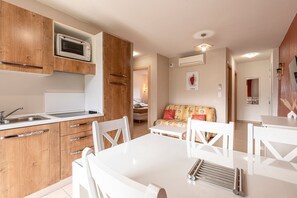 A modern kitchen with wooden cabinets, a built-in microwave, and a dining area with white furniture. - Chez Erna - Proche de Saint-Florent (Oletta)