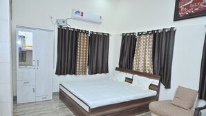 Ein Schlafzimmer mit einem Bett, einem Sessel, einem Kleiderschrank und einem Fenster mit Vorhängen.
