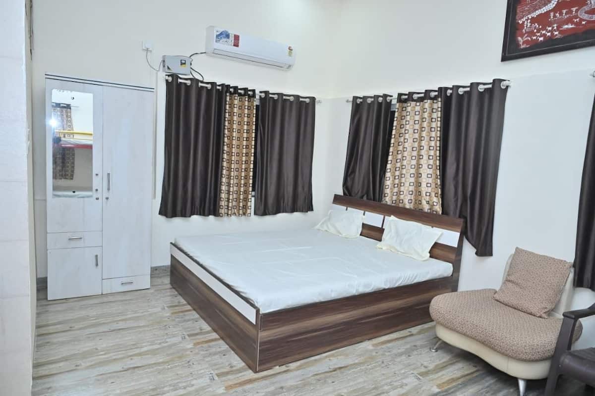 A bedroom with a bed, a chair, a wardrobe, and a window with curtains.