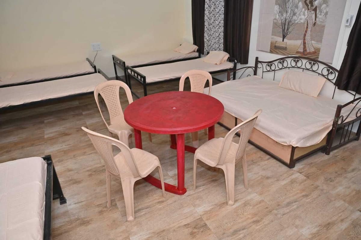 A room with a red table, four chairs, a sofa, and two beds.