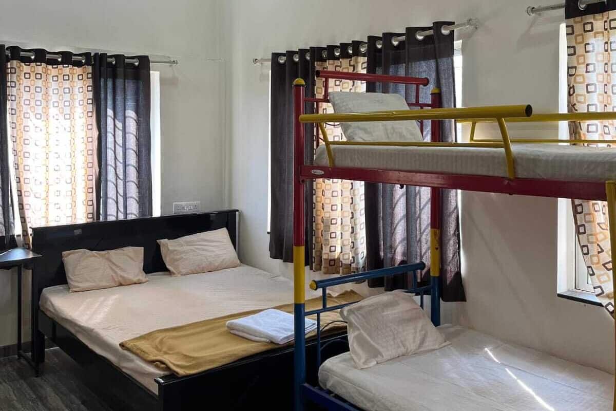 A dormitory room with bunk beds, a single bed, a desk, and a ceiling fan.