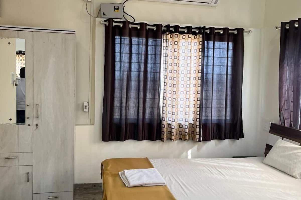 A hotel room with a bed, a wardrobe, a ceiling fan, and an air conditioning unit.