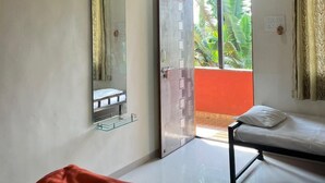 Ein Zimmer mit zwei Betten, einem Deckenventilator, einem Spiegel und einer Glastür, die auf einen Balkon mit Bepflanzung hinausführt.