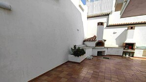 Un pati amb un paviment de rajoles, un forn exterior petit i una jardineria amb plantes.