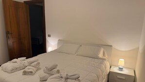 Un llit ben fet amb tovalloles arremolinades, una làmpada de nit i una tauleta de nit amb calaixos.