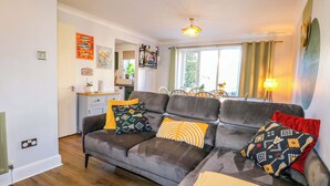 A modern living room with a grey sofa, patterned cushions, a small table, and a window with curtains. - Farnham Park Apartment (Farnham)