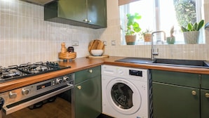 A kitchen with a gas stove, a built-in washing machine, and a window with plants. - Farnham Park Apartment (Farnham)