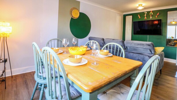 A dining area with a wooden table, chairs, and a television mounted on the wall. - Farnham Park Apartment (Farnham)