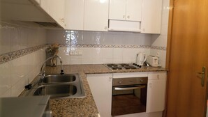 A compact kitchen with a sink, stove, and oven, white cabinets, and a wooden door. - 2 bedroom apartment in the center of Begur (H08) (Begur)