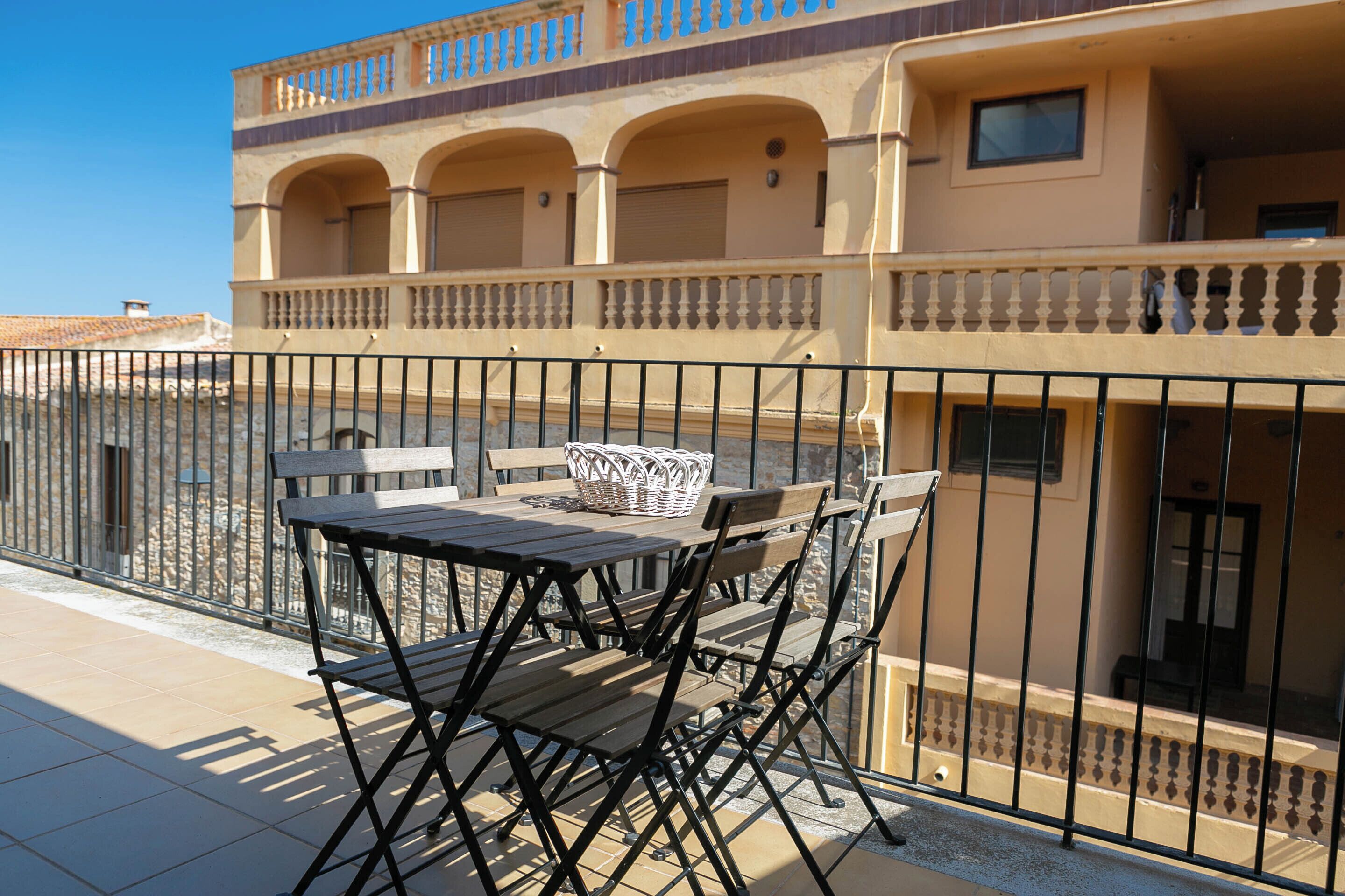 A balcony with a table and chairs, a basket, and a building with balconies and windows.