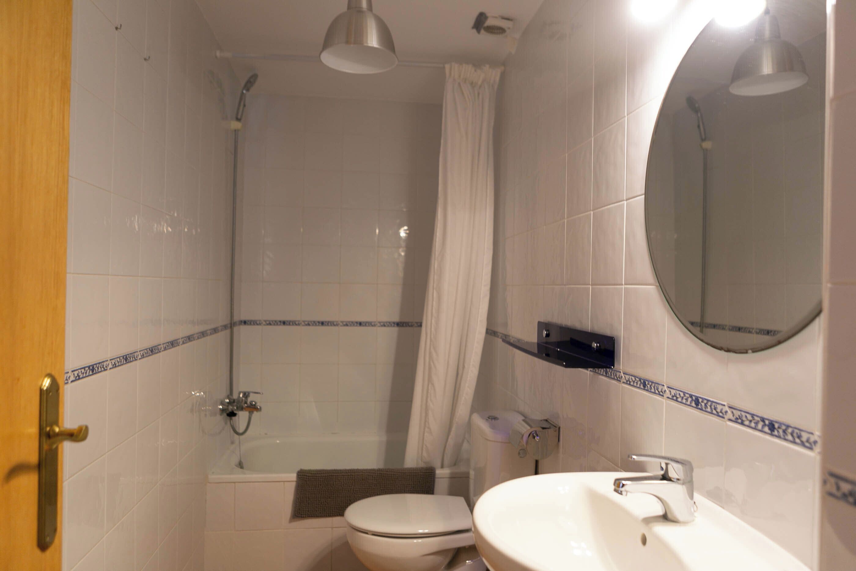 Een badkamer met douche, toilet, wastafel en spiegel.