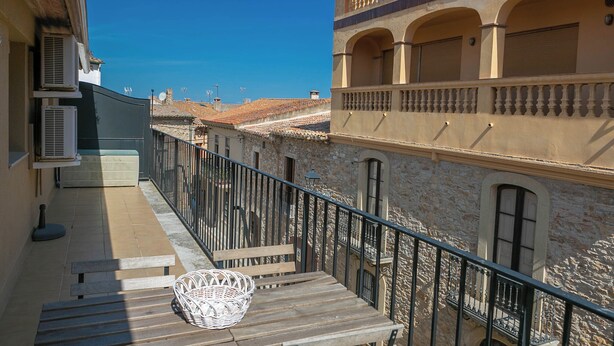 A balcony with a wicker basket, a wooden bench, and a view of a building with stone walls and arched windows. - 2 bedroom apartment in the center of Begur (H08) (Begur)