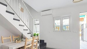 En trappe med hvide vægge og sorte detaljer, et spiseområde med bord og stole, samt et vindue med udsigt.