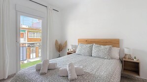 Et soveværelse med en seng, et natbord, en lampe, et vindue med gardiner og udsigt til bygninger.