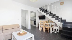 En stue med sofa, spisebord med stole, fjernsyn og trappe.