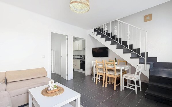 A living room with a sofa, a dining table with chairs, a TV, and a staircase. - Villa Almirante Torrecilla by South Costa (Nerja)