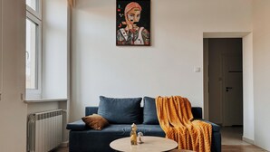 Ein Wohnzimmer mit einem dunkelblauen Sofa, einem runden Holztisch und einer leuchtend orangefarbenen Decke.