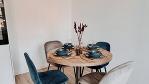 Una mesa redonda de comedor con platos azules, cubiertos negros y un florero con ramas secas.
