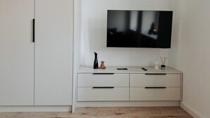 Ein schlichter Raum mit einem an der Wand befestigten Flachbildfernseher, einem weißen Schrank mit Schubladen und einem Holzboden.