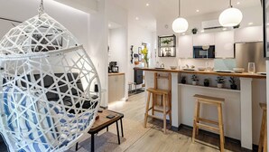 A modern kitchen with white cabinetry, a hanging light fixture, and a unique geometric hanging chair.