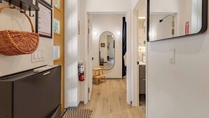 A hallway with a wicker basket, a fire extinguisher, a mirror, and a wooden stool.