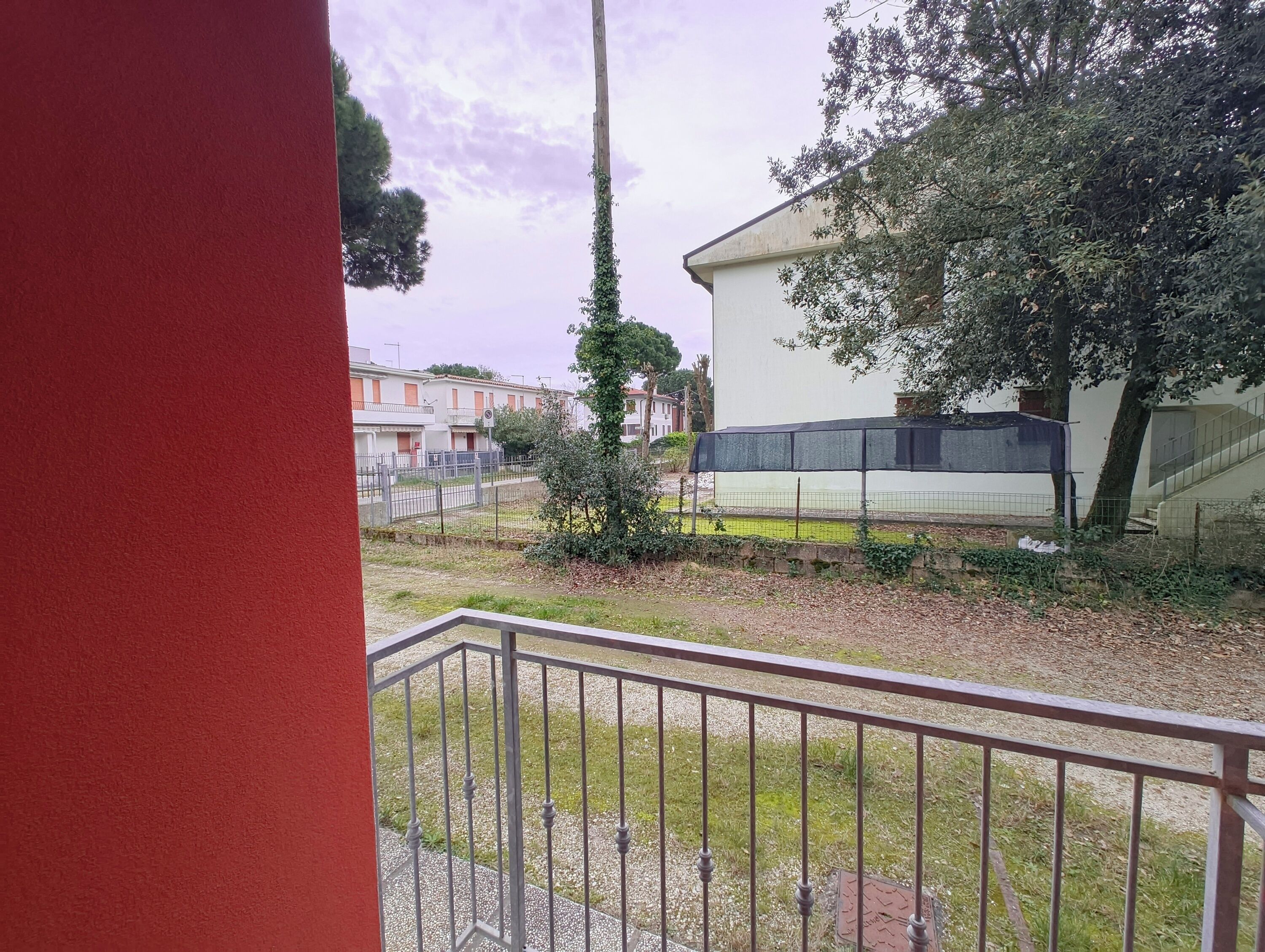 A residential area with a white building, a fenced garden, and a metal railing.