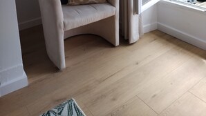 A corner room with a white armchair, a patterned pillow, a window with curtains, and a wooden floor. - 2 bedrooms, central location, quiet and sunny (Poitiers)
