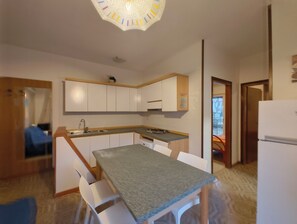 A modern kitchen with white cabinets, a grey countertop, and a dining area with white chairs. - Nice Flat in Rosolina Mare (Rosolina)