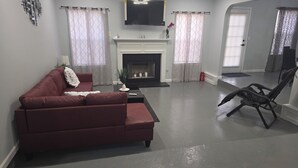 A living room with a red sofa, a fireplace, a television mounted above it, and a black chair.