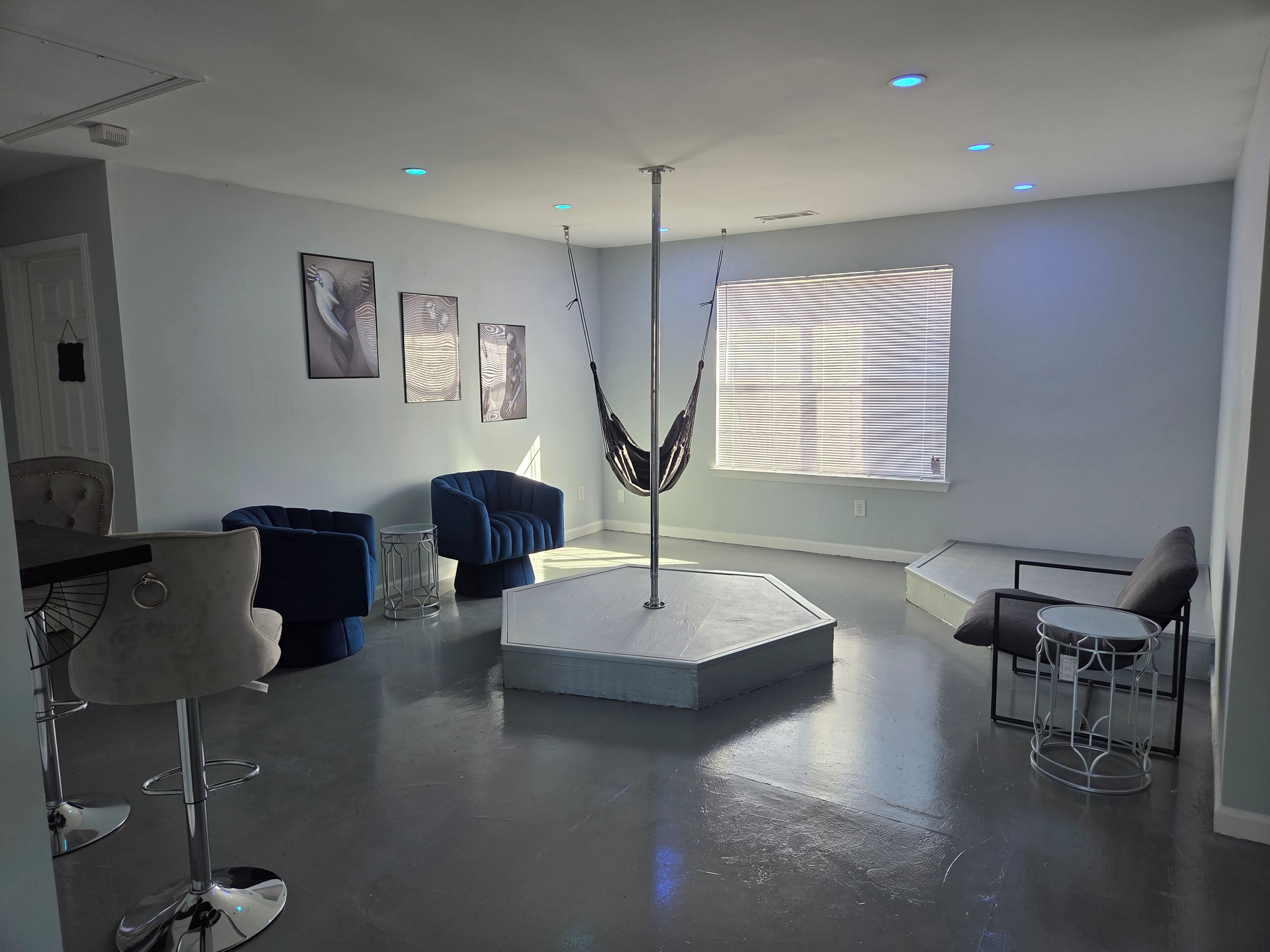 A modern living room with a central seating area, a hammock, and a dining area with a chair and table.