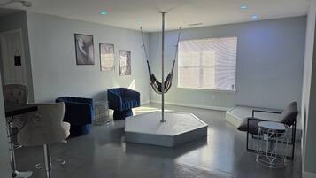 A modern living room with a central seating area, a hammock, and a dining area with a chair and table.
