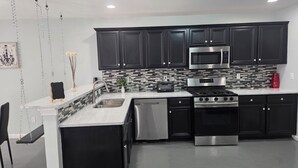 A modern kitchen with black cabinets, stainless steel appliances, a white countertop, and a hanging light fixture.