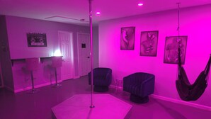 A room with a central pole, two chairs, a hanging chair, a small table, and a poster on the wall.